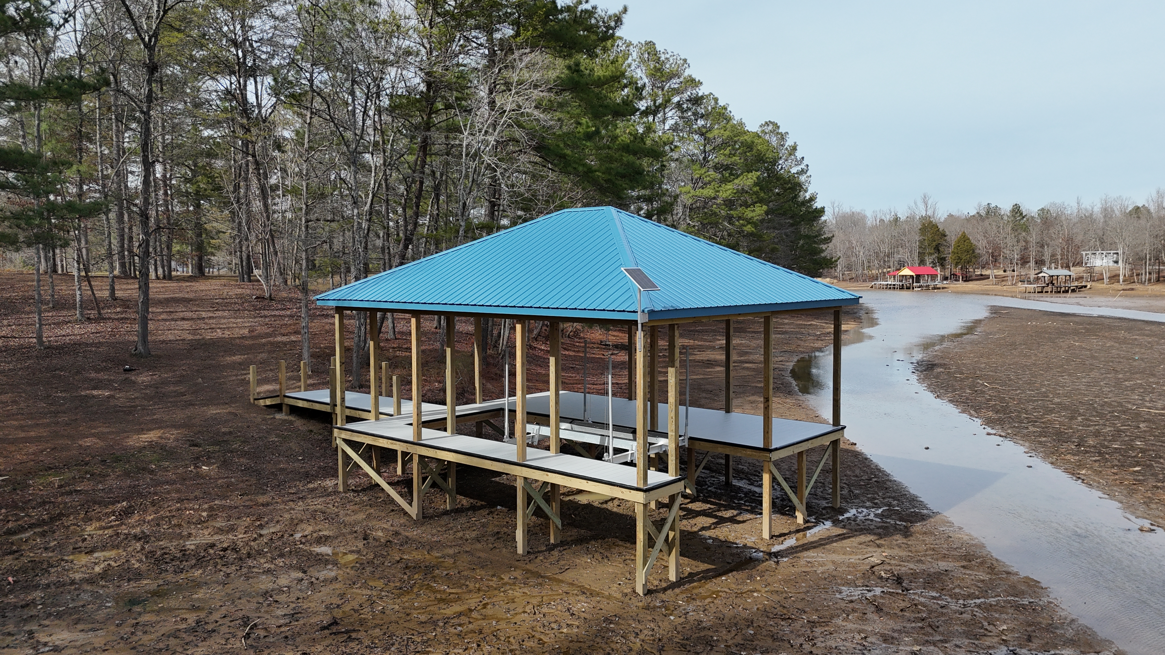 Open boathouse with bright blue metal roof on a low-water shoreline